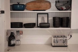 A kitchen with white cabinets, a blue pot, a wooden cutting board, black plates, a framed picture, a toaster, and a bottle of kombucha. - Mountain Bungalow near Mt Shasta and Waterfalls (Dunsmuir)