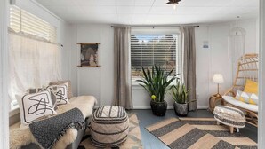 A modern living room with a sofa, ottomans, a chair, a lamp, and potted plants.