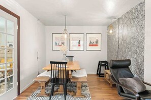 Ein Essbereich mit Holztisch, Stühlen und einer Bank. An der Wand hängen gerahmte Kunstwerke und auf dem Boden liegt ein Teppich mit Muster.