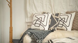 A bed with patterned pillows, a fluffy blanket, and a wooden floor lamp.