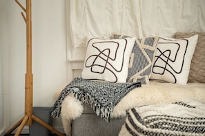 Un letto con cuscini decorati, una coperta soffice e una lampada da terra in legno.
