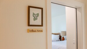 A hotel room with a bed, a framed botanical illustration, and a sign indicating the room name. - The Wildflower Inn (Gold Beach)