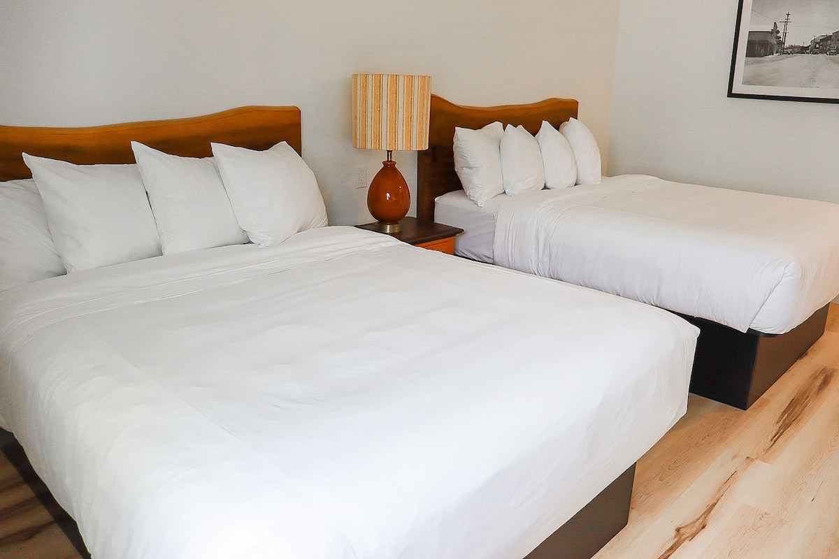 Une chambre d’hôtel avec deux lits, une tête de lit en bois, une table de chevet avec une lampe et un tableau encadré au mur.