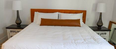 A neatly made bed with a wooden headboard, white bedding, and two bedside tables with lamps.