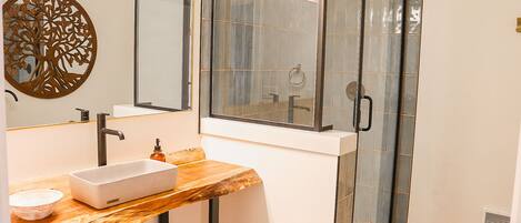 A bathroom with a wooden vanity, a white sink, a glass shower enclosure, and a decorative wall piece.