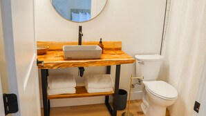 A bathroom with a wooden vanity, a sink, a toilet, and a mirror. - The Wildflower Inn (Gold Beach)