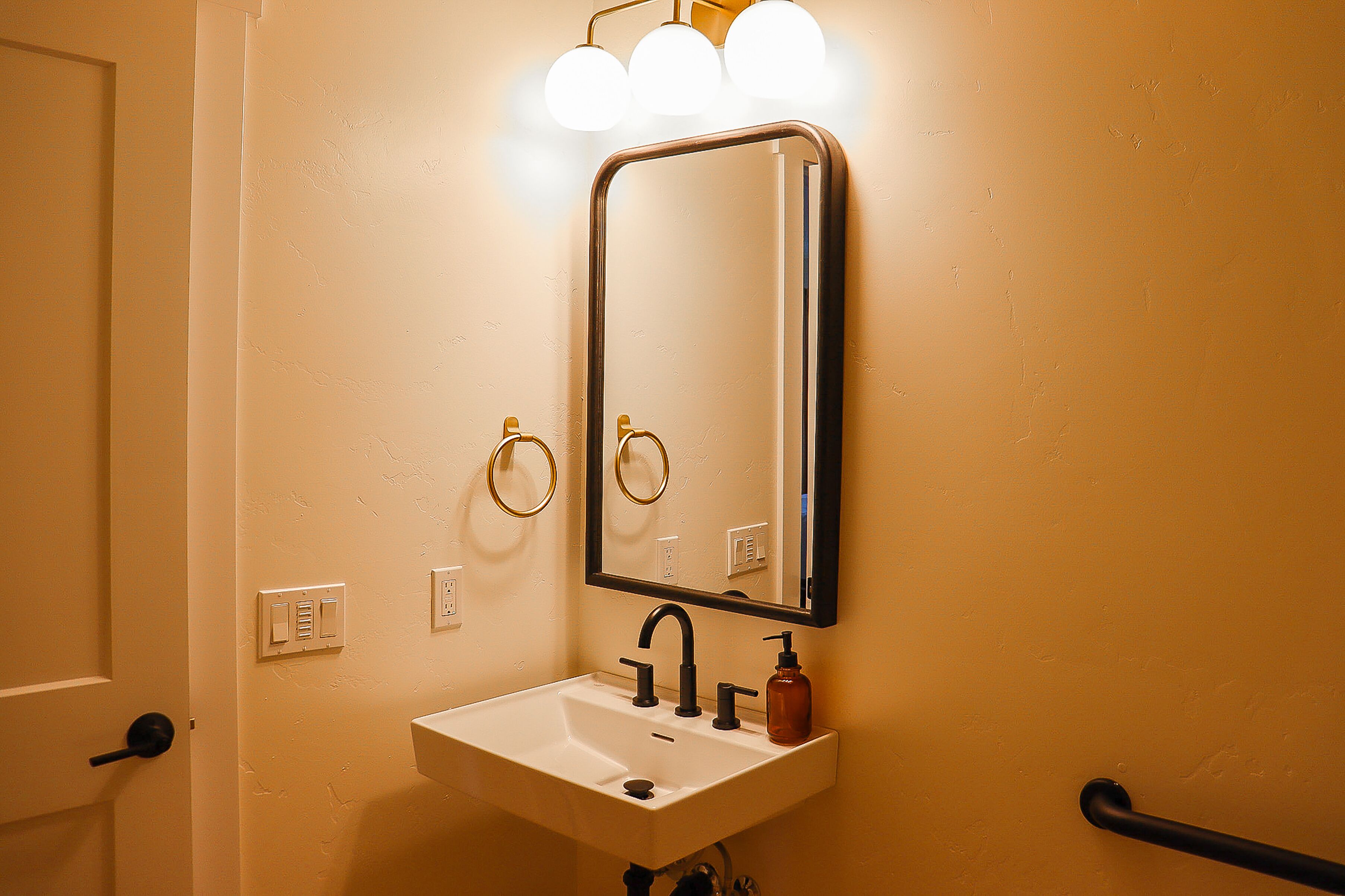 Un baño con un lavabo blanco, un espejo y una lámpara sobre él.