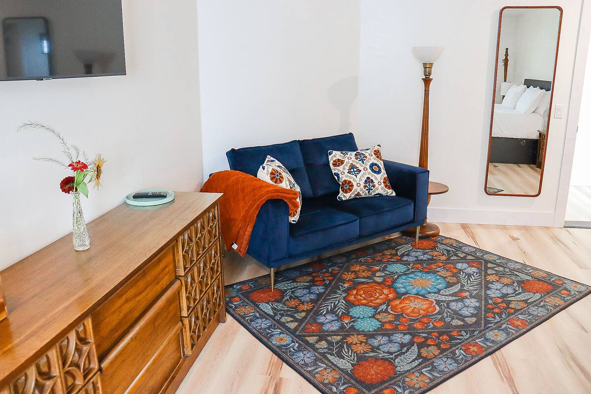 Un salon avec un canapé bleu, des coussins décoratifs, une table d’appoint en bois sur laquelle est posé un vase, et un tapis à motifs.
