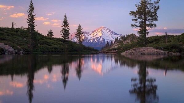 Un lago de montaña con reflejos, rodeado de árboles y un cielo despejado.