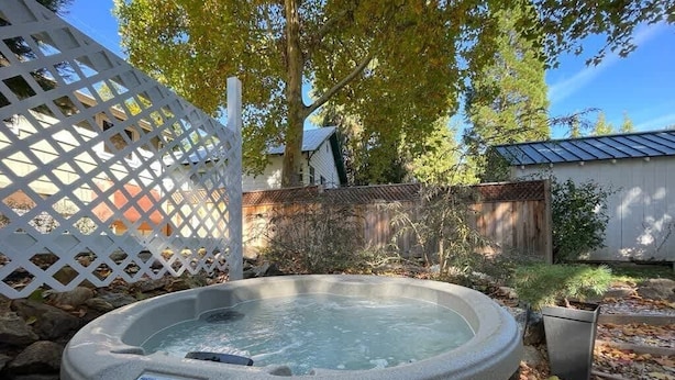 A hot tub in a backyard with a wooden fence, trees, and a shed. - Picturesque Garden Retreat w/Deck With Hot Tub (Dunsmuir)