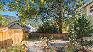 A backyard with a wooden fence, a stone pathway, and a small garden area. - Picturesque Garden Retreat w/Deck With Hot Tub (Dunsmuir)
