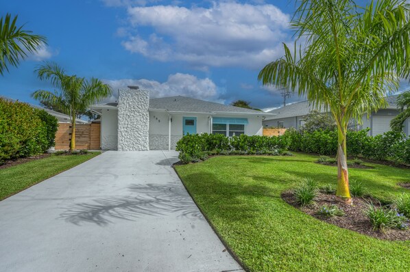 A modern house with a stone pillar, a blue door, and a well-maintained lawn with palm trees. - Vacation Home Near the Beach! (Naples)