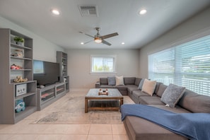 A modern living room with a sectional sofa, a flat-screen TV, built-in shelving, and a ceiling fan. - Vacation Home Near the Beach! (Naples)