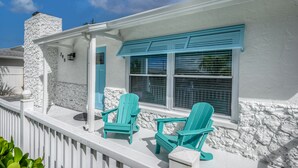 Une véranda couverte avec deux fauteuils Adirondack turquoise et une cheminée en pierre.