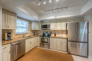 A modern kitchen with stainless steel appliances, beige cabinetry, and a granite countertop. - Vacation Home Near the Beach! (Naples)