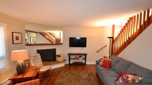 Una sala de estar con chimenea, televisor, sofá y escalera.