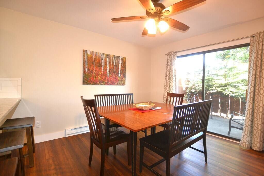 Un coin repas avec une table et des chaises en bois, un ventilateur de plafond, un tableau accroché au mur et une porte-fenêtre coulissante donnant sur un espace extérieur.