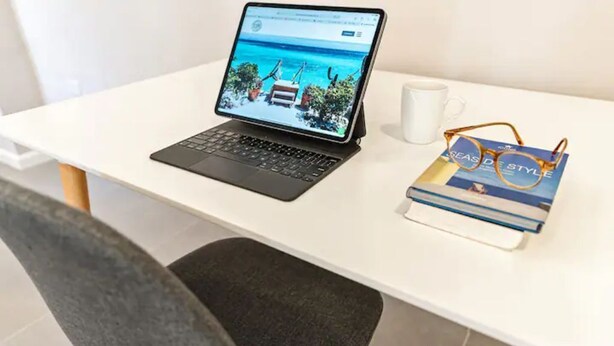 Een laptop op een wit bureau, met een boek met de titel 'Seaside Style' en een paar brillen ernaast.