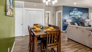 A dining area with a wooden table set for four, a sofa, and a painting on the wall. - Lighthouse-Themed, Fastest WiFi, 2 King Beds Home (Medford)
