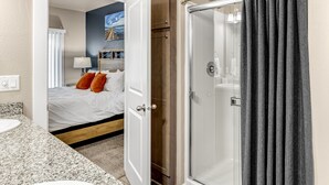 A bathroom with a shower, a sink, and a bed visible through an open door. - Lighthouse-Themed, Fastest WiFi, 2 King Beds Home (Medford)