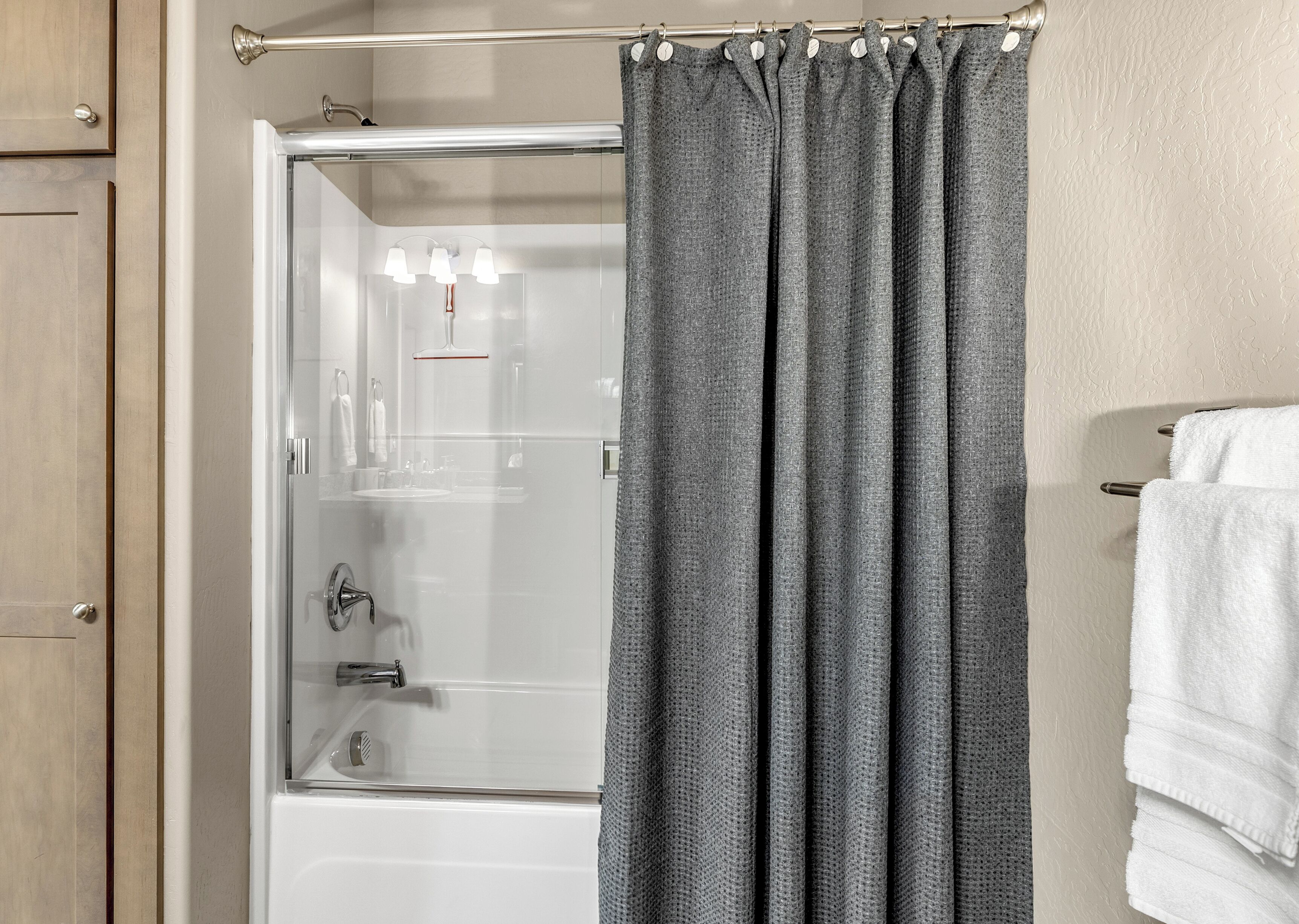 A bathroom with a shower, a glass door, and a towel rack with white towels.