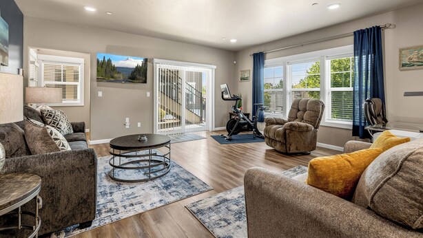 A spacious living room with a large window, a treadmill, and a view of a staircase leading to a balcony. - Lighthouse-Themed, Fastest WiFi, 2 King Beds Home (Medford)