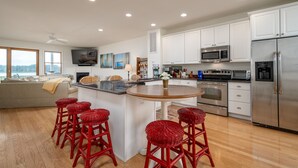 Una cocina moderna con gabinetes blancos, electrodomésticos de acero inoxidable y una isla central con taburetes de mimbre rojo.