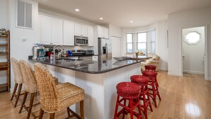Una cocina moderna con armarios blancos, una isla central con taburetes y un comedor con mesa redonda.