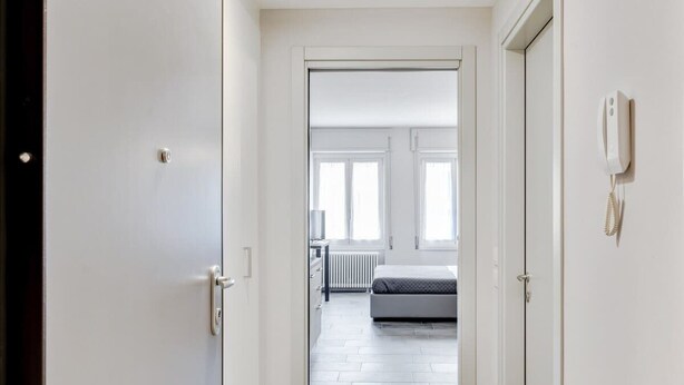 A hallway leading to a bedroom with a bed, a radiator, and a phone on the wall.