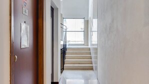 A hallway with a wooden door, a staircase, and a window at the end.