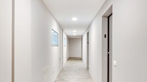 A modern, well-lit hallway with white walls and a light wood floor, leading to a door with a keypad lock.
