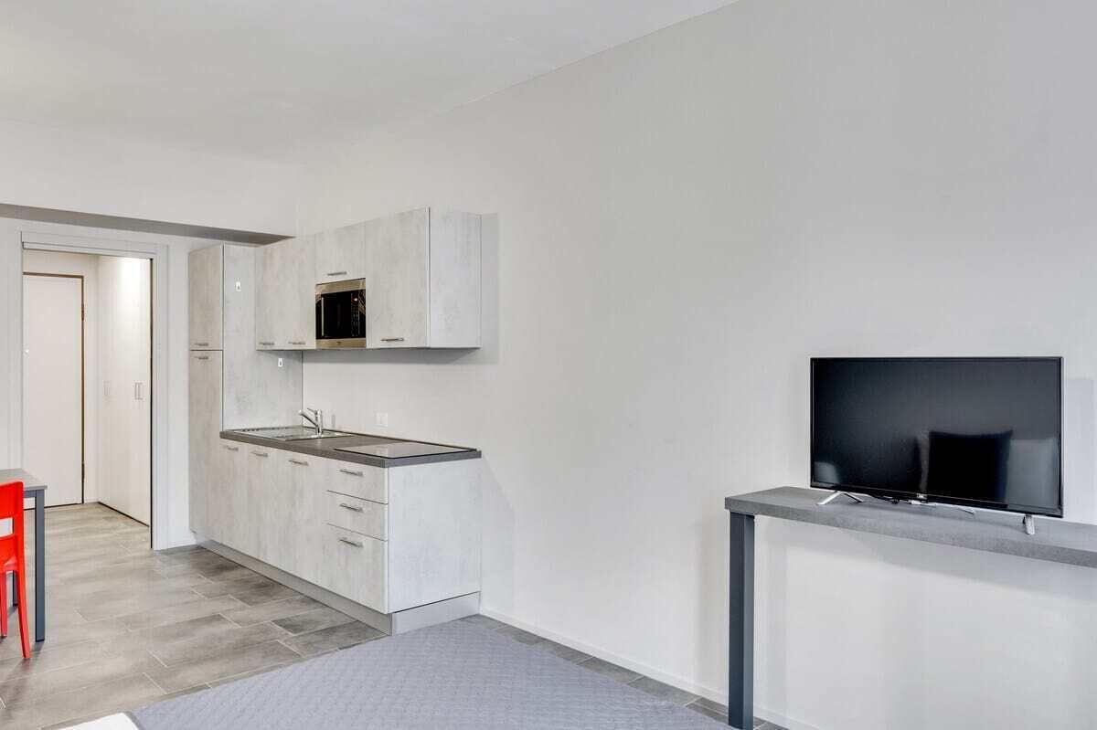 A modern kitchen with grey cabinets, a microwave, and a flat-screen TV mounted on a grey console.