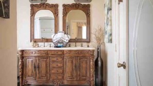 A bathroom with a wooden vanity, two mirrors, and a vase of dried plants. - Charming King Suite•Historic Mansion Near Monterey (Salinas)