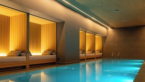 Una piscina interior moderna con zonas de estar de madera e iluminación empotrada.