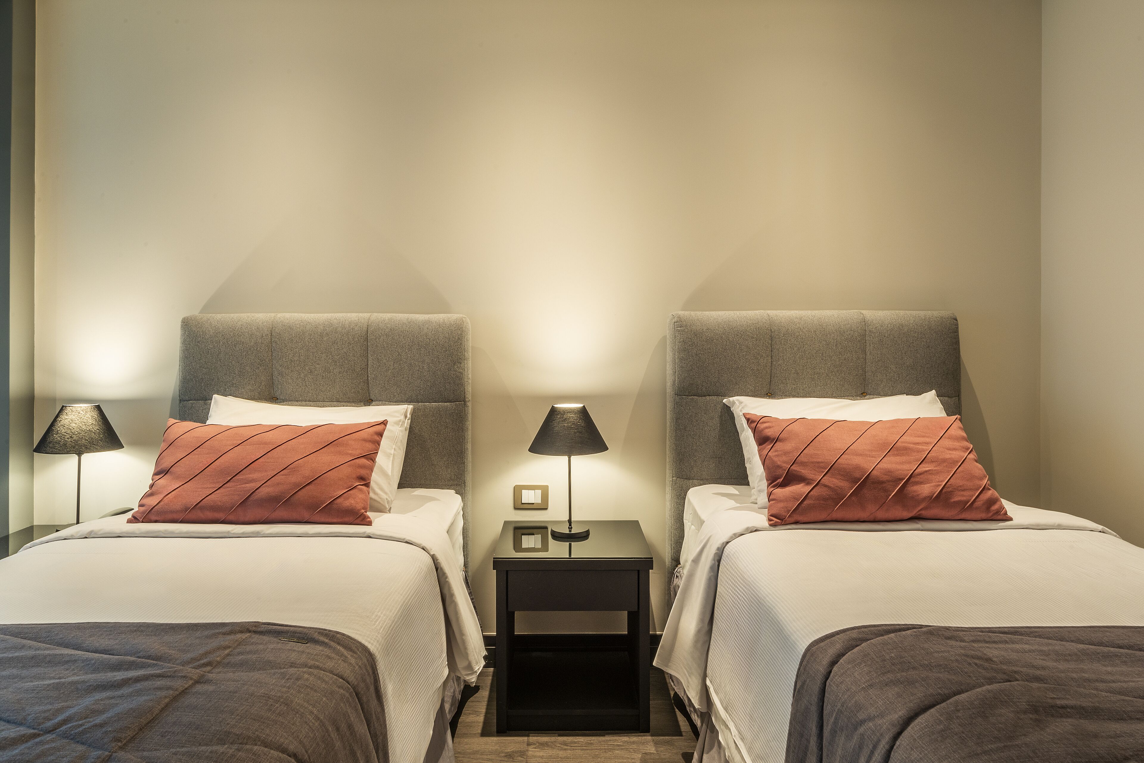 A twin room with two beds, a nightstand with a lamp, and a small table with a lamp.