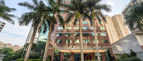 A multi-story hotel with a modern facade, palm trees in front, and a clear sky.