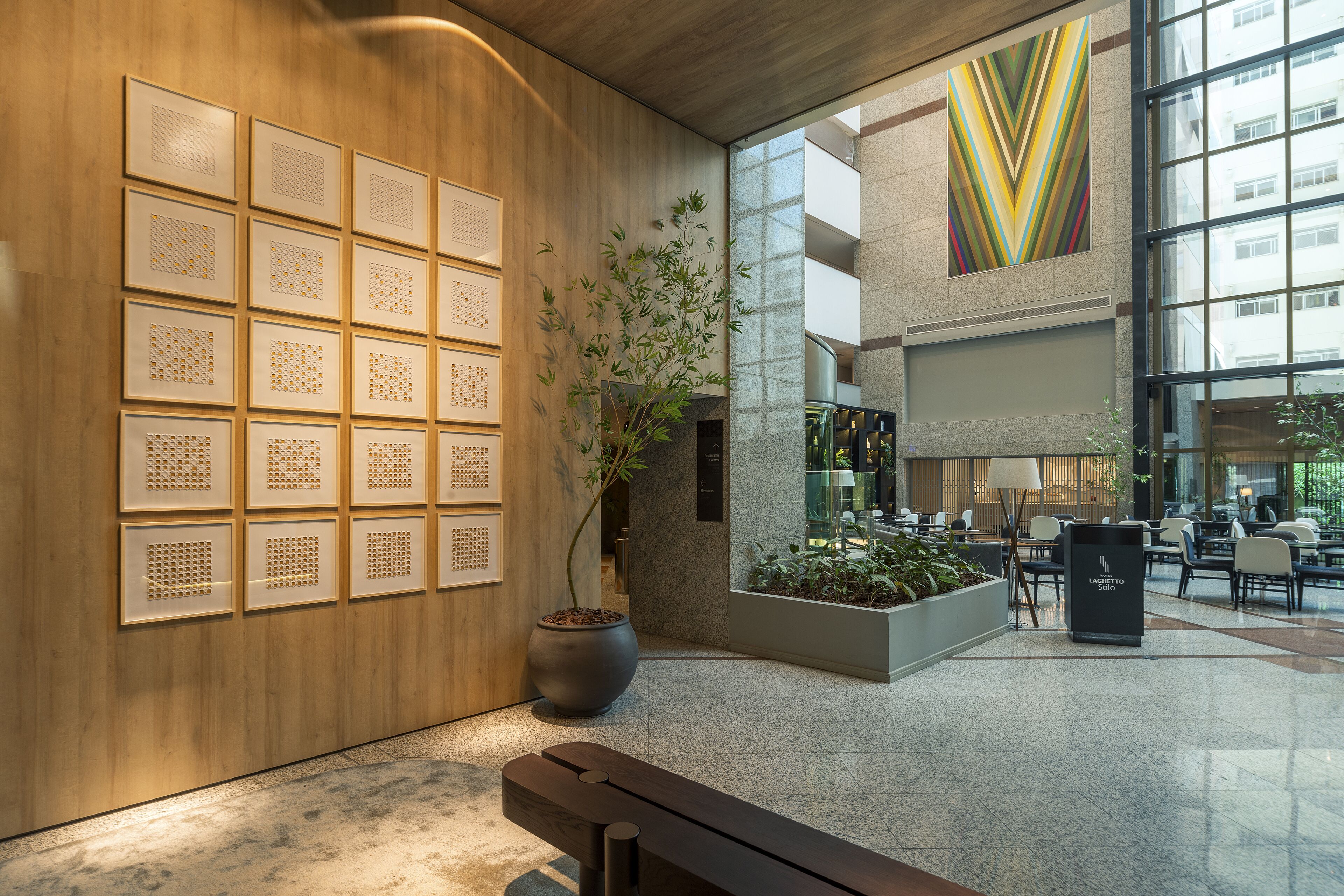A modern lobby with a wooden wall, a potted plant, a bench, and a seating area with tables and chairs.