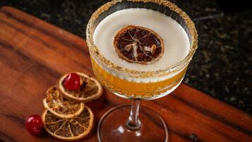 Um cocktail num copo com borda salgada e rodela de laranja desidratada, sobre uma superfície de madeira com rodelas de laranja secas e cereja.