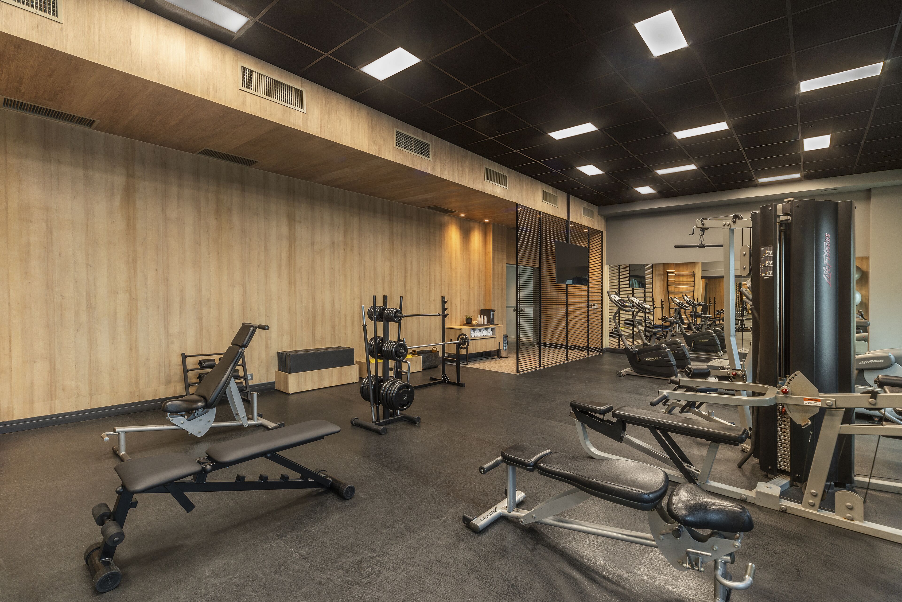 A gym with various exercise equipment, wooden walls, and a ceiling with square lights.
