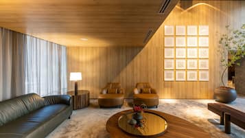 Ein modernes Wohnzimmer mit Ledersofa, zwei Sesseln, einem Couchtisch aus Holz und einer Wand mit strukturierten Paneelen.