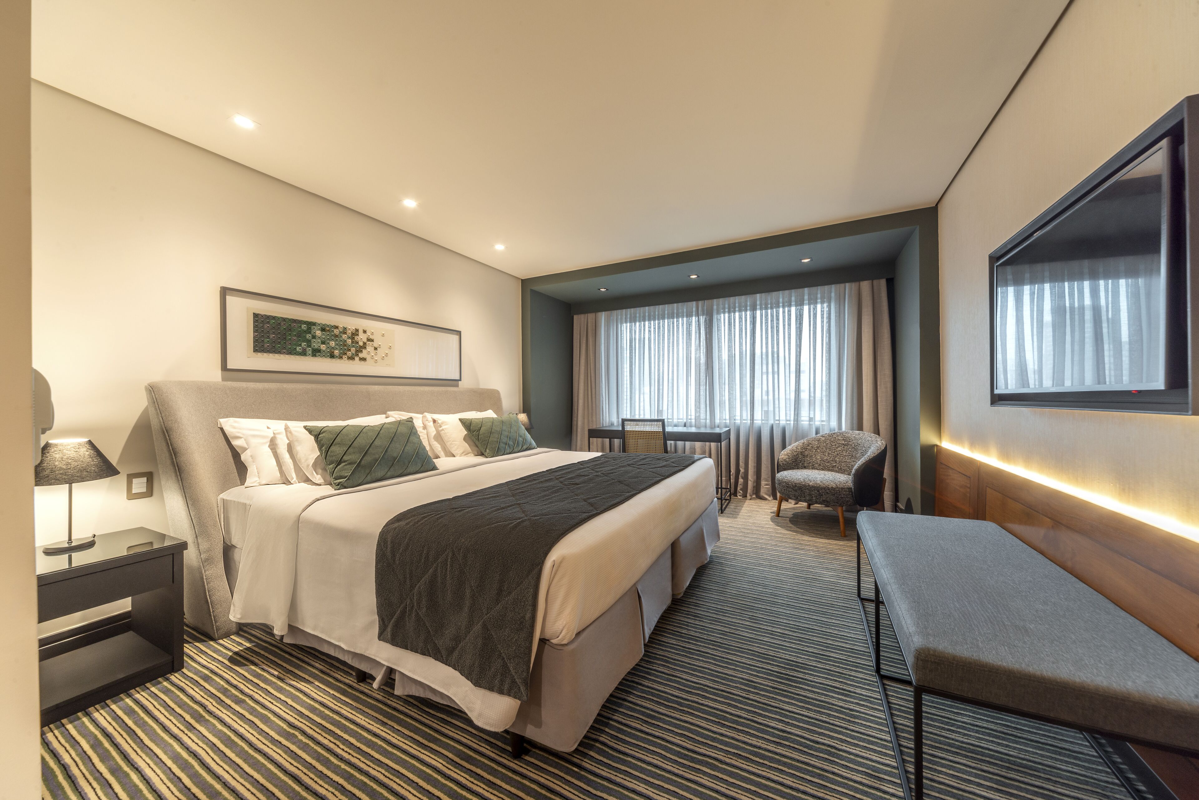 Una habitación de hotel moderna con una cama grande, un escritorio, una silla y un banco.