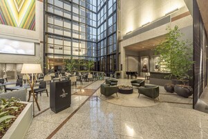 Un'ampia hall con soffitto alto, grandi finestre e una zona salotto centrale con divani e tavolino.
