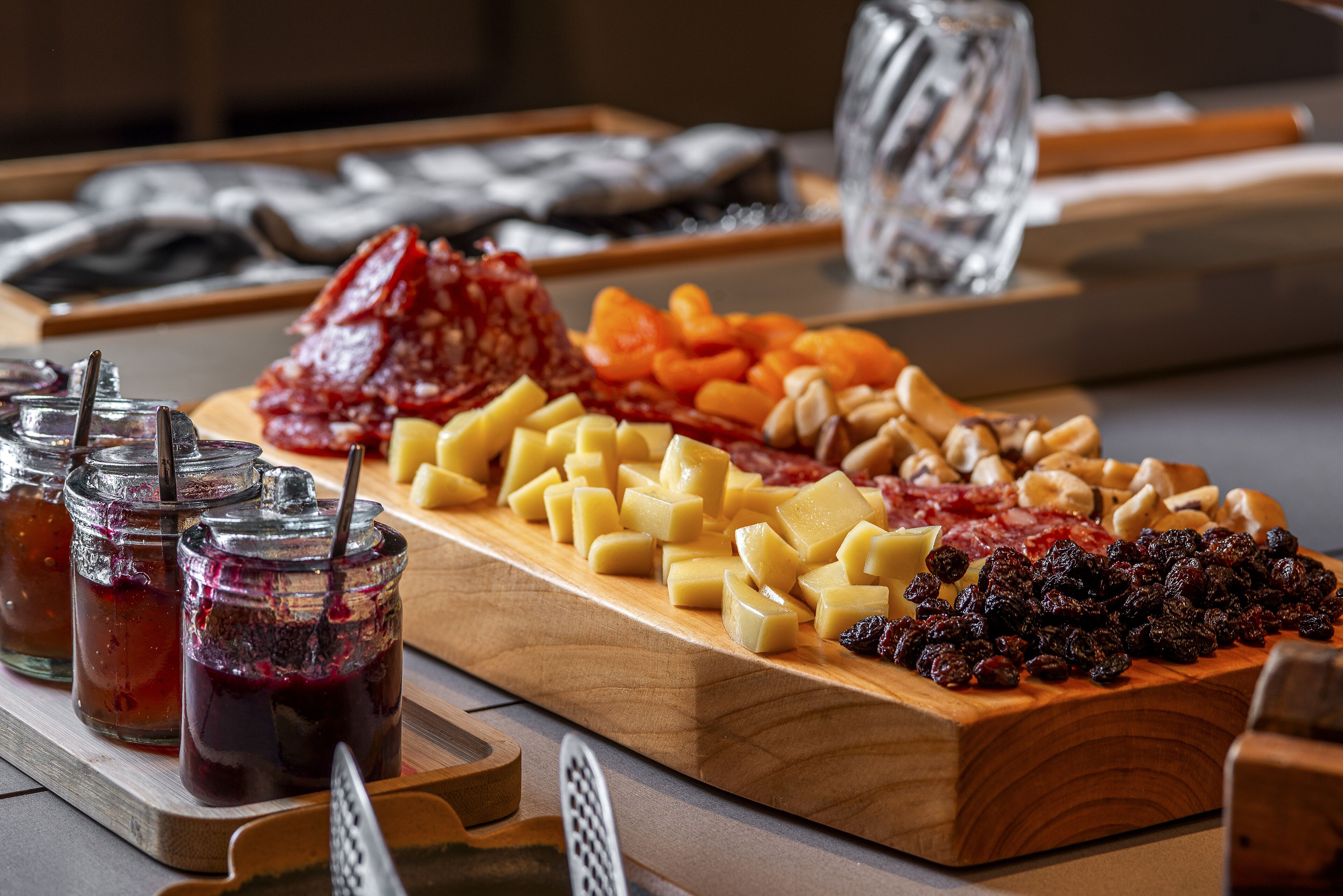 A wooden board with various cheeses, fruits, and jams.