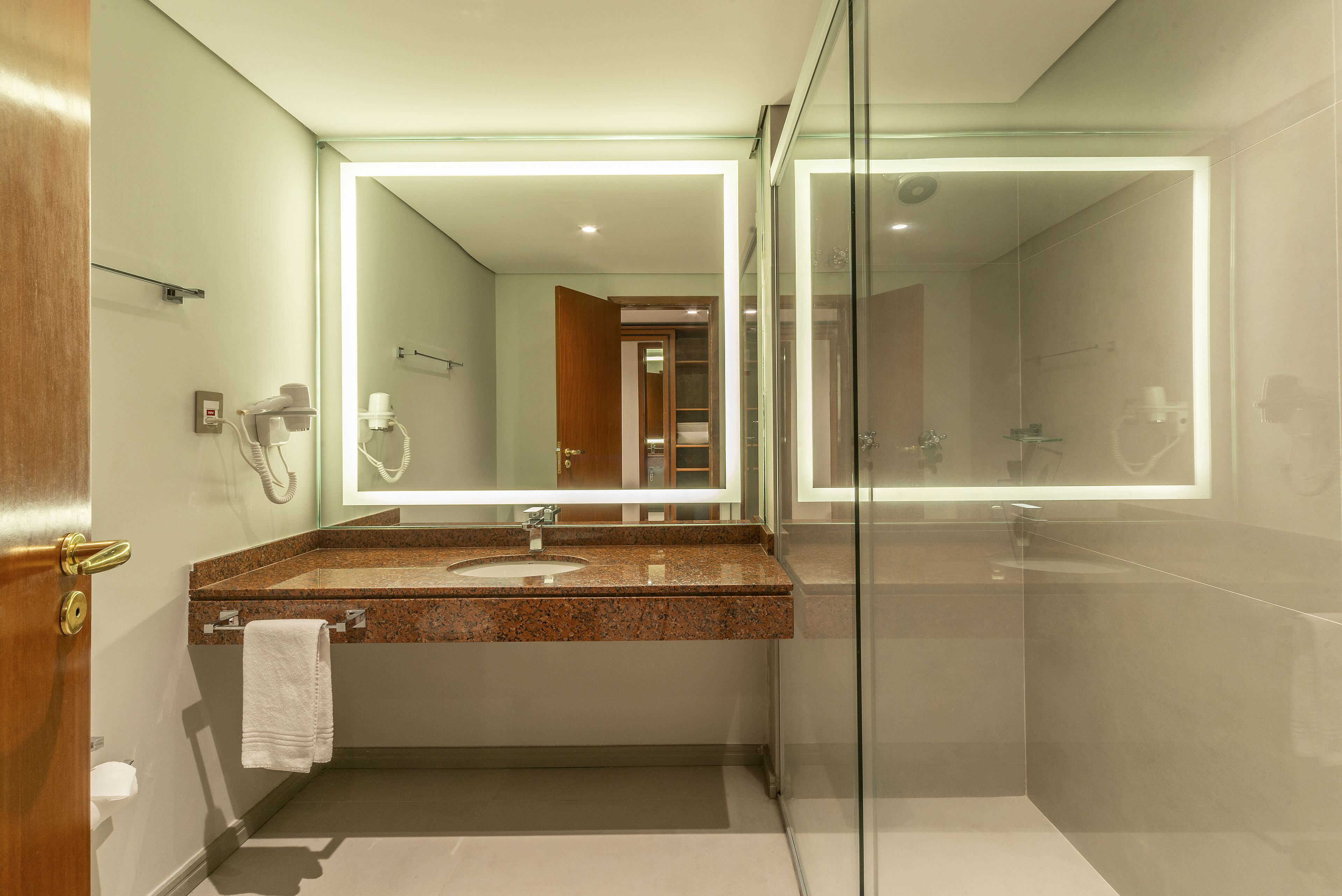 Un baño moderno con lavamanos de granito, cabina de ducha de vidrio y un espejo grande.