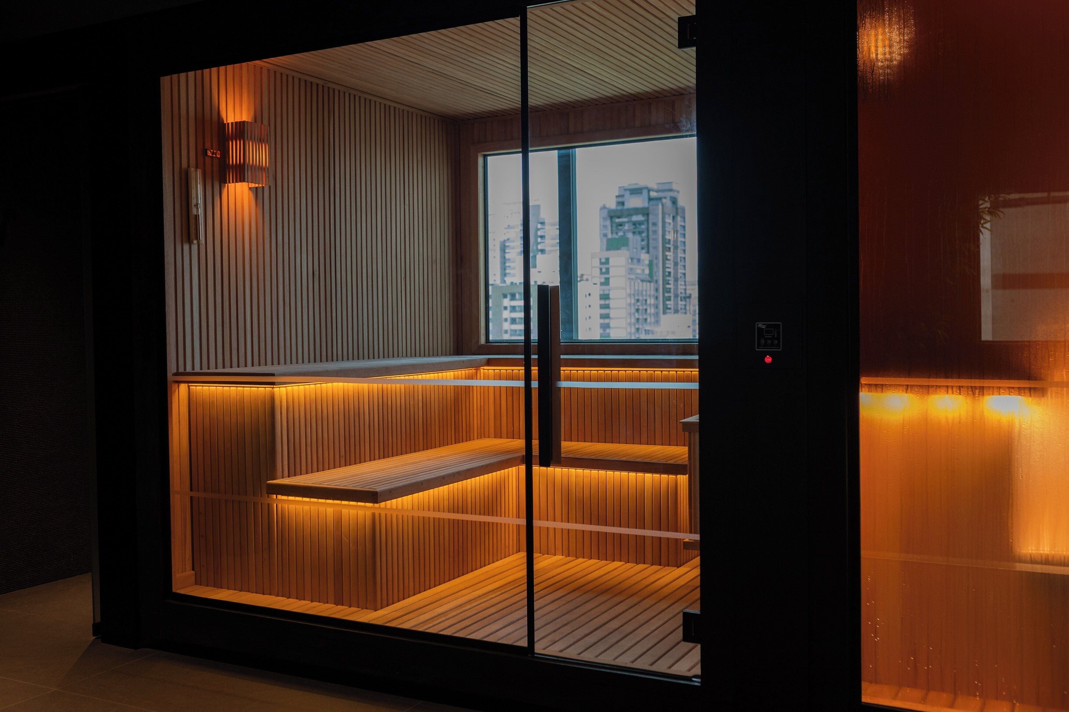 Een moderne sauna met houten latten en een glazen deur, met uitzicht op de stad.