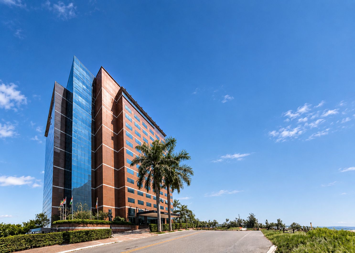 Un hotel moderno con fachada de vidrio, sección de ladrillo rojo y entrada bordeada de palmeras.