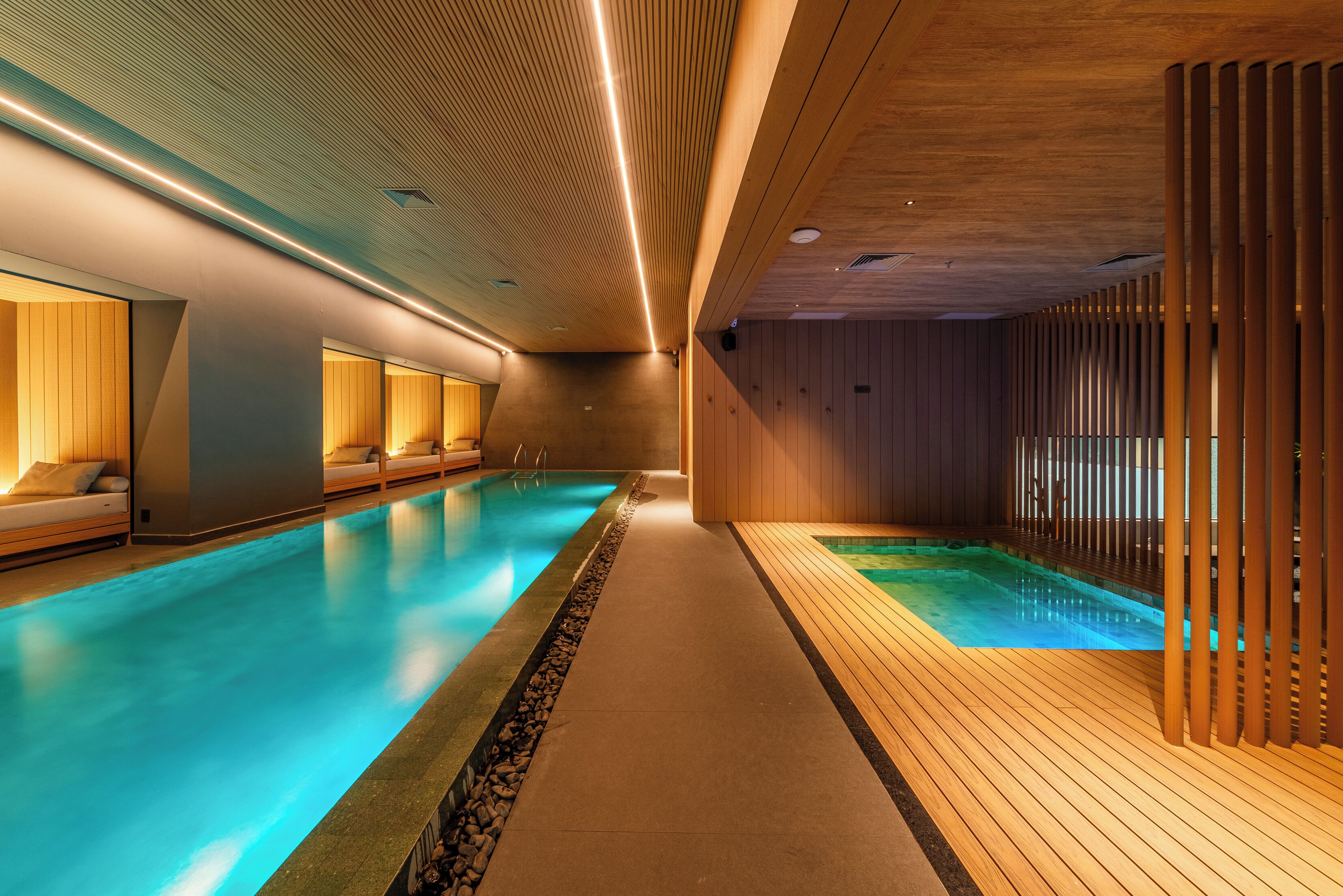 A modern indoor swimming pool with wooden paneling and a long corridor.