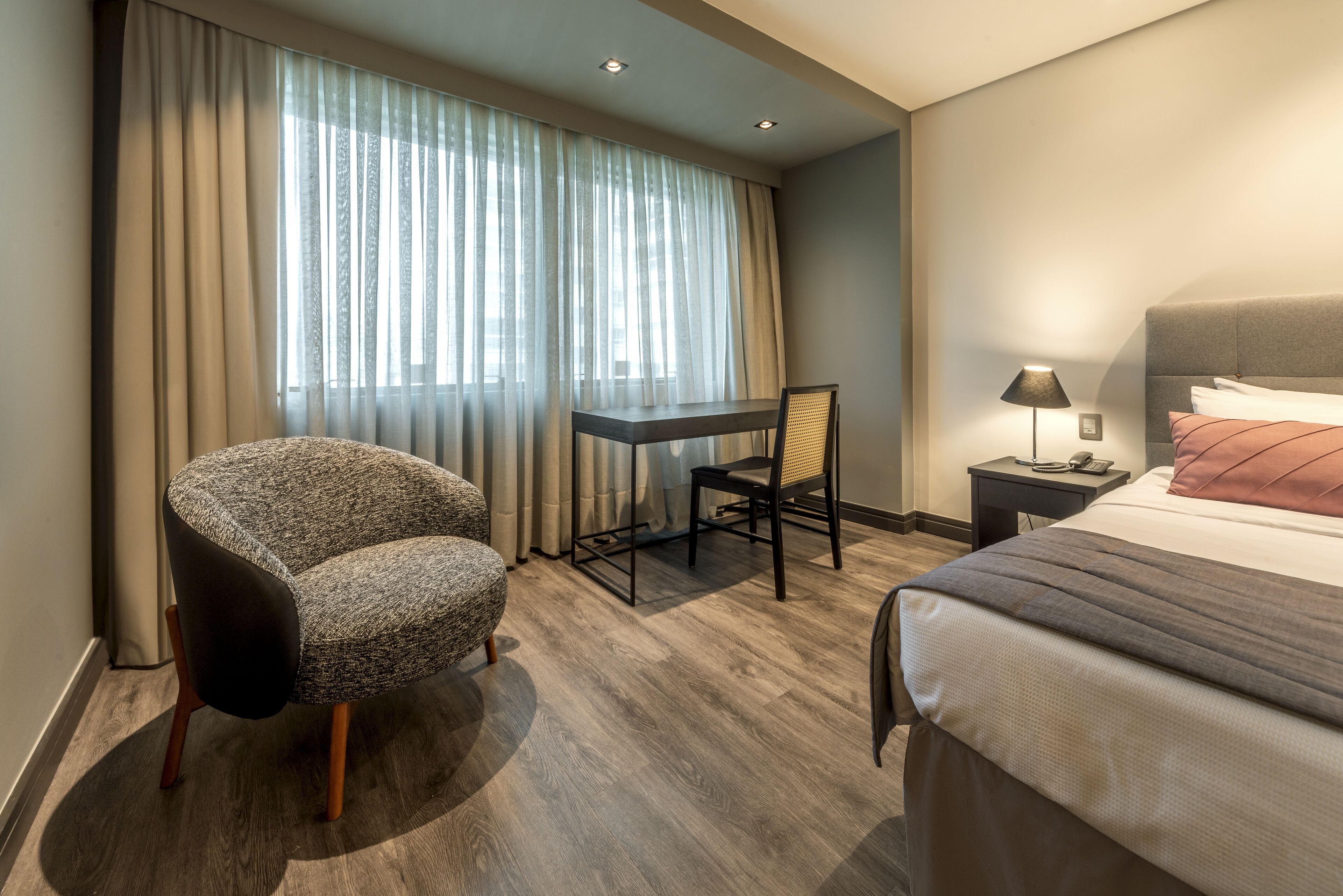 Ein Hotelzimmer mit Bett, Schreibtisch, Stuhl und Nachttisch mit Lampe.