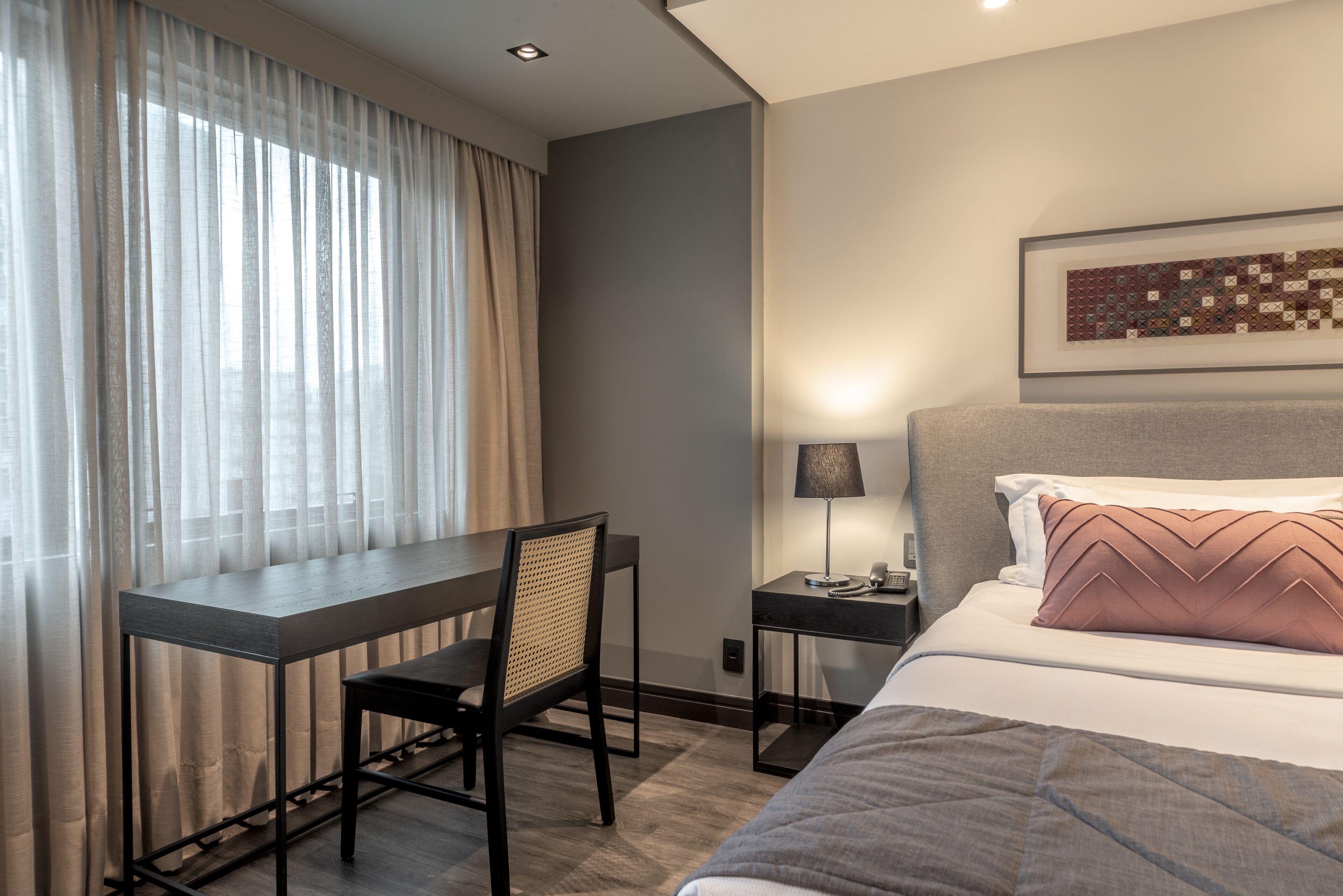 Una habitación de hotel con cama, escritorio, silla, mesita de noche y lámpara.