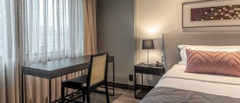 Una habitación de hotel con cama, escritorio, silla, mesita de noche y lámpara.